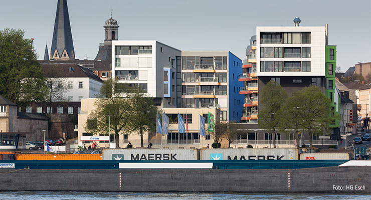 Wohn- und Geschäftsbebauung am Brassertufer in Bonn. Vier Gebäude mit eigenständigem Charakter gruppieren sich um ein hochwassersicheres Plateau mit einem grünen Hof.